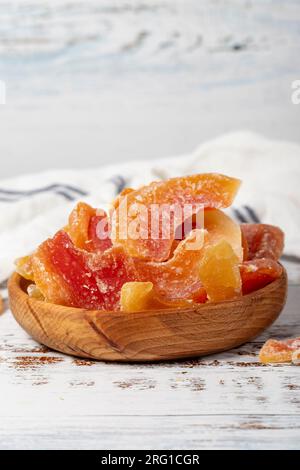 Getrocknete Papaya-Scheiben in einer Holzschüssel. Sonnengetrocknete, natürliche Papaya-Scheiben auf weißem Holzhintergrund. Schließen Stockfoto