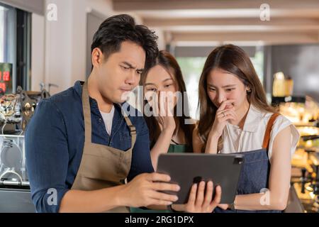 Drei Begegnungen des Barista Entrepreneur Teams im Café. Junge asiatische, männliche und weibliche Café-Mitarbeiter, die ernsthaft Gespräche mit einem Tablet-Computer führen Stockfoto
