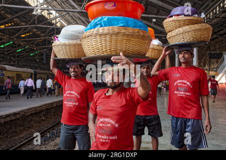 Gepäckträger am Chhatrapati Shivaji Maharaj Terminus in Mumbai, Indien, mit Körben auf dem Kopf, die darauf warten, dass ein lokaler Zug ihre Waren befördert Stockfoto