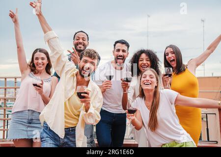 Porträt einer großen Gruppe junger erwachsener Freunde, die am Wochenende eine Geburtstagsparty auf dem Dach mit Weingläsern feiern. Multirassische Männer und Frauen, die Spaß haben und zusammen lächeln und ihre Freundschaft genießen. Hochwertiges Foto Stockfoto