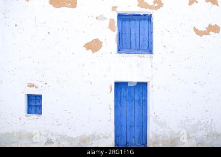 Weiße Wand mit blauer Holztür und zwei Fenstern Stockfoto