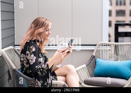 Frau, die SMS schreibt und Wein trinkt, während sie draußen auf der Terrasse sitzt Stockfoto