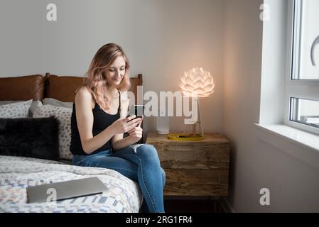 Frau, die im Bett sitzt und SMS auf dem Smartphone schreibt Stockfoto