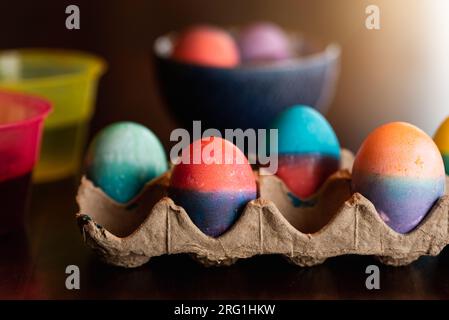 Nahaufnahme gefärbter Ostereier in einem Karton und in einer Schüssel auf einem Tisch. Stockfoto