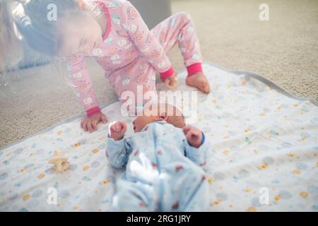 Die ältere Schwester sitzt, spielt mit ihrem neugeborenen Bruder. Stockfoto