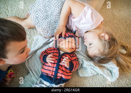 Ältere Geschwister kuscheln mit ihrem neuen kleinen Bruder. Stockfoto