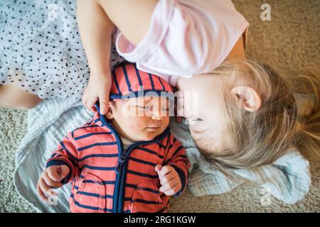 Eine ältere Schwester umarmt ihren jüngeren, neugeborenen Bruder Stockfoto