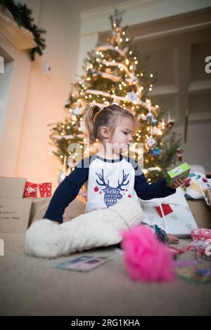 Das junge Mädchen öffnet seinen Strumpf unter dem Weihnachtsbaum Stockfoto