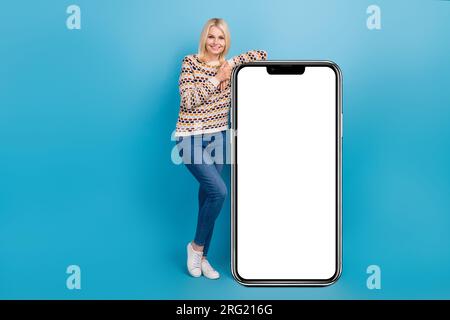Ein großes Porträt einer Frau mit positivem Alter zeigt ein riesiges leeres Telefon auf blauem Hintergrund Stockfoto