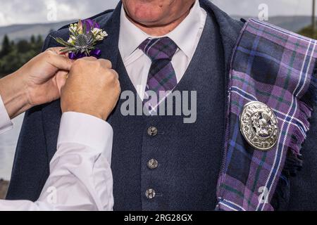 Bräutigam in traditionellem schottischem Kleid bereitet sich auf die Hochzeit vor und bekommt Hilfe mit dem Knopflöcher Stockfoto