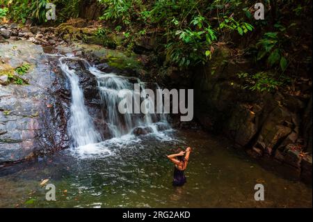 Eine Frau, die in einem Pool am Fuß eines kleinen Wasserfalls steht. Osa-Halbinsel, Costa Rica. Stockfoto