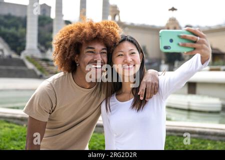 Lächelndes junges Paar, das draußen ein Selfie mit dem Telefon macht. Fröhliches Paar, das lächelt und draußen ein Foto macht. Stockfoto