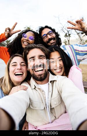 Vertikales Porträt einer vielfältigen Gruppe von Freunden, die ein Selfie auf der Straße machen. Fröhliche, multiethnische Gruppe junger Hipster, die draußen ein Foto machen Stockfoto