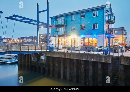 Ein Café- und Apartmenthaus am Hafen neben einer Hebebrücke, bei Sonnenuntergang gesehen, neben dem Yachthafen in Exmouth, Devon, Großbritannien. Stockfoto