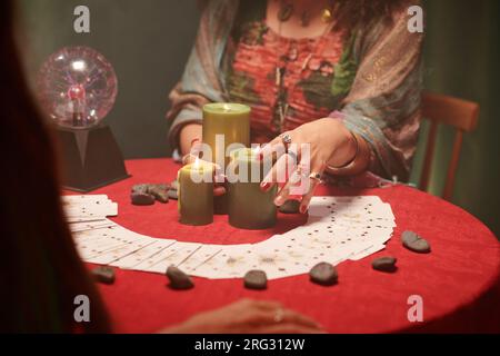 Hände des Wahrsagers, der brennende Wachskerzen auf den Tisch legt und Tarotkarten verteilt Stockfoto