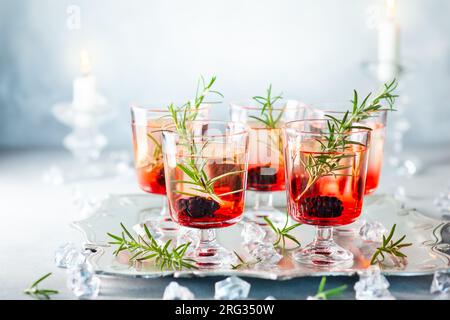 Winterbeercocktails mit Brombeerlikör und Gin zu Weihnachten oder Neujahr. Serviert mit frischen Brombeeren und Rosmarin auf dem silbernen Tablett. Stockfoto