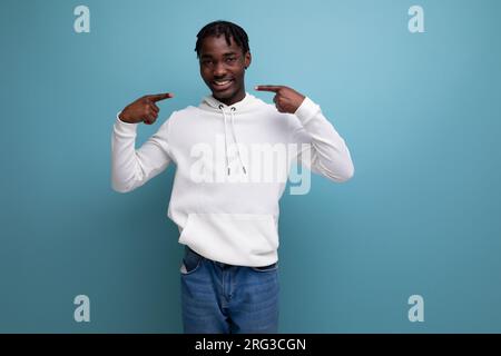Porträt eines optimistischen Mannes mit Dreadlocks in einem weißen Kapuzenpulli auf blauem Hintergrund Stockfoto