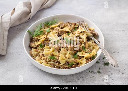 Traditionelles jüdisches Gericht Kasha Varnishkes: Buchweizen, Pasta, Champignon-Pilze, gebratene Zwiebeln mit Kräutern auf grauem, strukturiertem Hintergrund, vegane Speisen, t Stockfoto