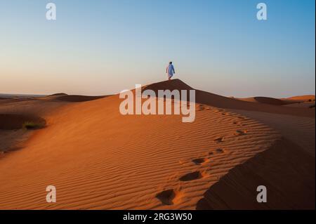 Ein Omani, der bei Sonnenuntergang entlang eines Sanddünenrückens läuft. Wahiba Sands, Arabische Halbinsel, Oman. Stockfoto