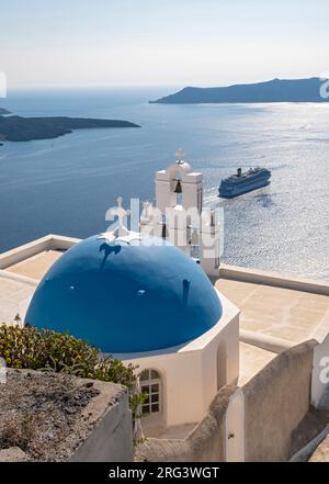 Berühmte Kirche mit blauer Kuppel und Glocke (drei Glocken von Fira) mit Costa Fortuna Kreuzfahrtschiff, katholische Dormitionskirche, Firostefani, Santorin, Griechenland Stockfoto