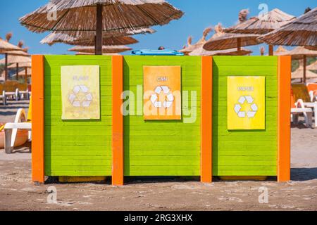 Müllcontainer zum Sammeln von Recyclingmaterial. Abfalltrennung. Separates Abfallsammelglas, Papier und Dose am Strand in Stockfoto