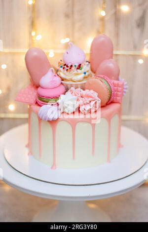 Wunderschöner Kuchen dekoriert mit geschmolzener rosa Schokolade, Makronen, Baiser, Kuchenpops und Süßigkeiten auf festlichem Hintergrund Stockfoto