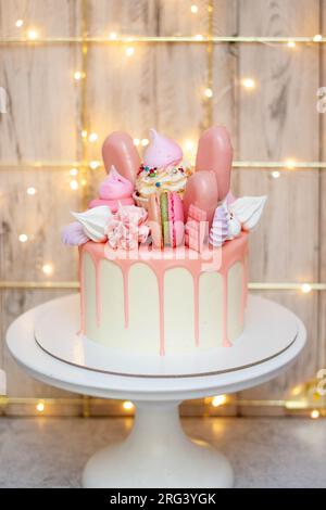 Wunderschöner Kuchen dekoriert mit geschmolzener rosa Schokolade, Makronen, Baiser, Kuchenpops und Süßigkeiten auf festlichem Hintergrund Stockfoto