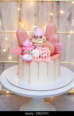 Wunderschöner Kuchen dekoriert mit geschmolzener rosa Schokolade, Makronen, Baiser, Kuchenpops und Süßigkeiten auf festlichem Hintergrund Stockfoto