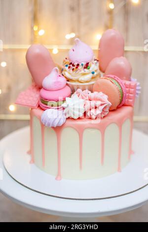 Wunderschöner Kuchen dekoriert mit geschmolzener rosa Schokolade, Makronen, Baiser, Kuchenpops und Süßigkeiten auf festlichem Hintergrund Stockfoto