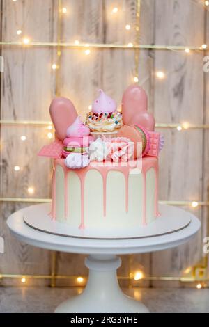 Wunderschöner Kuchen dekoriert mit geschmolzener rosa Schokolade, Makronen, Baiser, Kuchenpops und Süßigkeiten auf festlichem Hintergrund Stockfoto