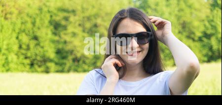 30-jährige brünette Frau mit langen Haaren, die eine Sonnenbrille in der Natur trägt. Stockfoto