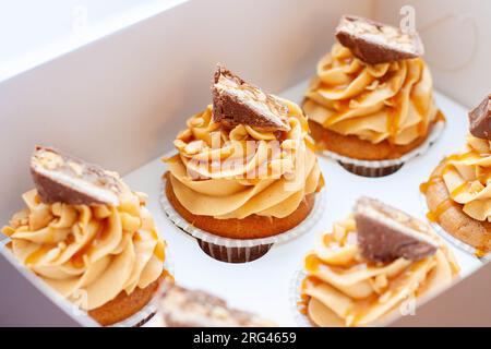 Wunderschöne Cupcakes mit Erdnussbutter, gesalzenem Karamell und Schokoriegel auf einer Geschenkbox aus Karton Stockfoto