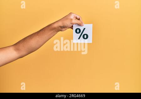 Die Hand eines Weißen, der Papier mit Prozentmarkierung auf isoliertem gelben Hintergrund hält Stockfoto