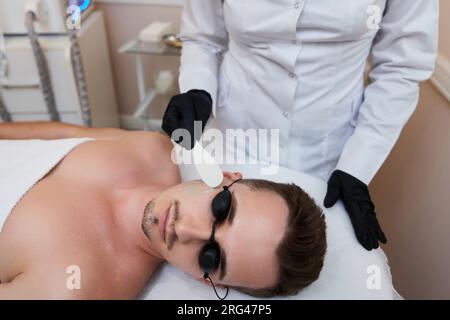 Junger Mann, der im Schönheitssalon epiliert wird. Laser-Haarentfernungsverfahren Stockfoto