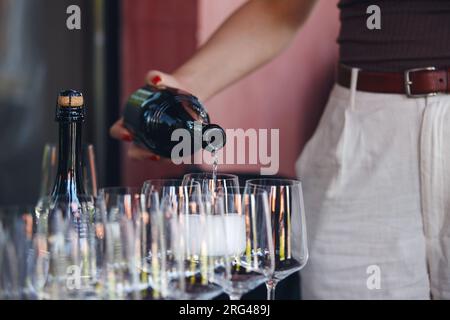 Die Kellnerin gießt Sekt auf das Glas auf dem Bartisch, Nahaufnahme ohne Gesicht. Stockfoto