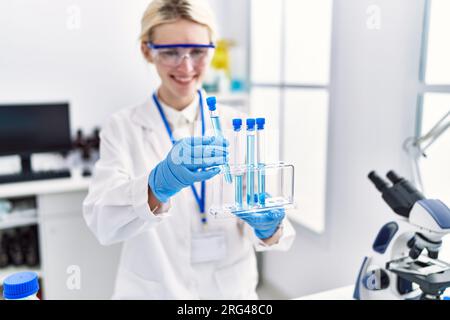Junge blonde Wissenschaftlerin, die Reagenzgläser im Labor analysiert Stockfoto