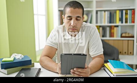 Junger hispanischer Student, der Touchpad benutzt und an der Bibliotheksuniversität studiert Stockfoto