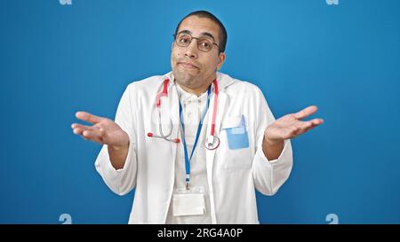 Junger hispanischer Arzt, ahnungslos über isolierten blauen Hintergrund Stockfoto