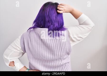 Eine große Frau mit lila Haaren, die über weißem Hintergrund steht und über Zweifel nachdenkt, mit der Hand auf dem Kopf Stockfoto