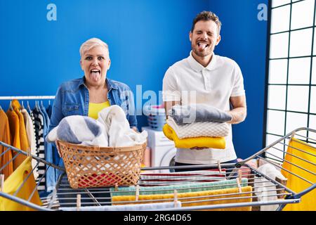 Hispanische Mutter und Sohn hängen Kleider an der Wäscheleine und stecken die Zunge mit lustigem Ausdruck heraus. Stockfoto