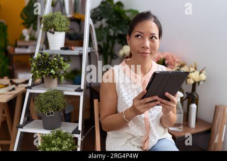 Eine junge asiatische Floristin, die selbstbewusst mit dem Touchpad im Blumenladen lächelt Stockfoto