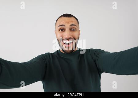 Lächelnder junger Mann, der Selfie auf grauem Hintergrund macht Stockfoto