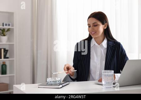 Frau mit langem Zigarettenhalter zum Rauchen am Arbeitsplatz im Büro Stockfoto