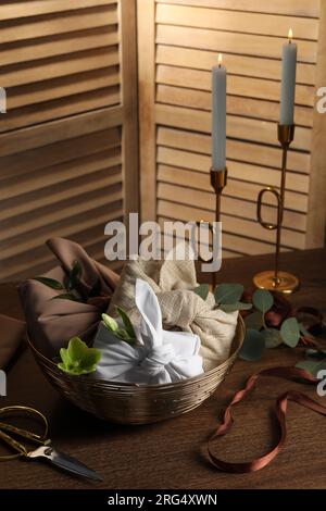 Furoshiki-Technik. Geschenke verpackt in verschiedenen Stoffen, Blumen, Band und Schere auf Holztisch Stockfoto