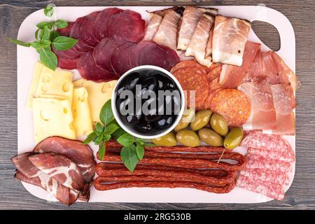 Blick von oben auf Wurstscheiben, Speck, Hamon, Käse und Oliven mit grünem Basilikum. Snacks aus nächster Nähe. Stockfoto