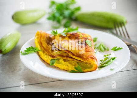 Gebratenes Omelett mit Zucchini, auf einem Teller auf einem Holztisch. Stockfoto