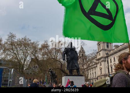 London, Großbritannien, 2023. Grüne Flagge mit dem Symbol des Aussterbens Rebellion am Parliament Square, mit der Statue von Churchill im Hintergrund Stockfoto