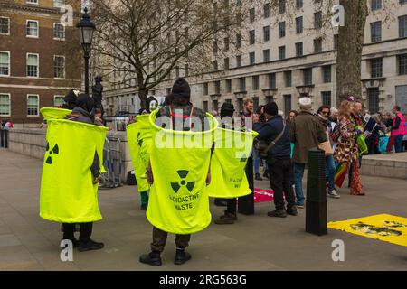 London, Großbritannien, 2023. In der Parliament Street tragen Klimaschutzaktivisten gelbe Scheinfässer, die radioaktiven Abfall lesen Stockfoto