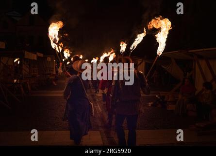 Menschen in mittelalterlichen Kleidern und gepanzerten Ritter mit brennenden Fackeln während einer Feuerprozession in tiefer Nacht. Stockfoto