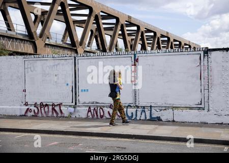 Eine Frau mit einem Kleinkind läuft an der Graffiti-Wand vorbei, die angeblich vom rat weiß gestrichen wurde. China Disciant, eine antichinesische Aktivistengruppe der Kommunistischen Partei in London, malt Graffiti an die umstrittene Wand in Brick Lane. Eine Gruppe chinesischer Studenten vom Royal College of London (RCA) hat die Mauer mit den 12 Grundwerten des Sozialismus während der Kulturrevolution über das Wochenende weiß gestrichen. Ihre Aktionen haben eine heftige Debatte zwischen lokalen Künstlern und chinesischen Gemeinschaften ausgelöst und die Verbreitung prochinesischer Propaganda in Frage gestellt. Die Mauer wurde als Repräsentant bezeichnet Stockfoto